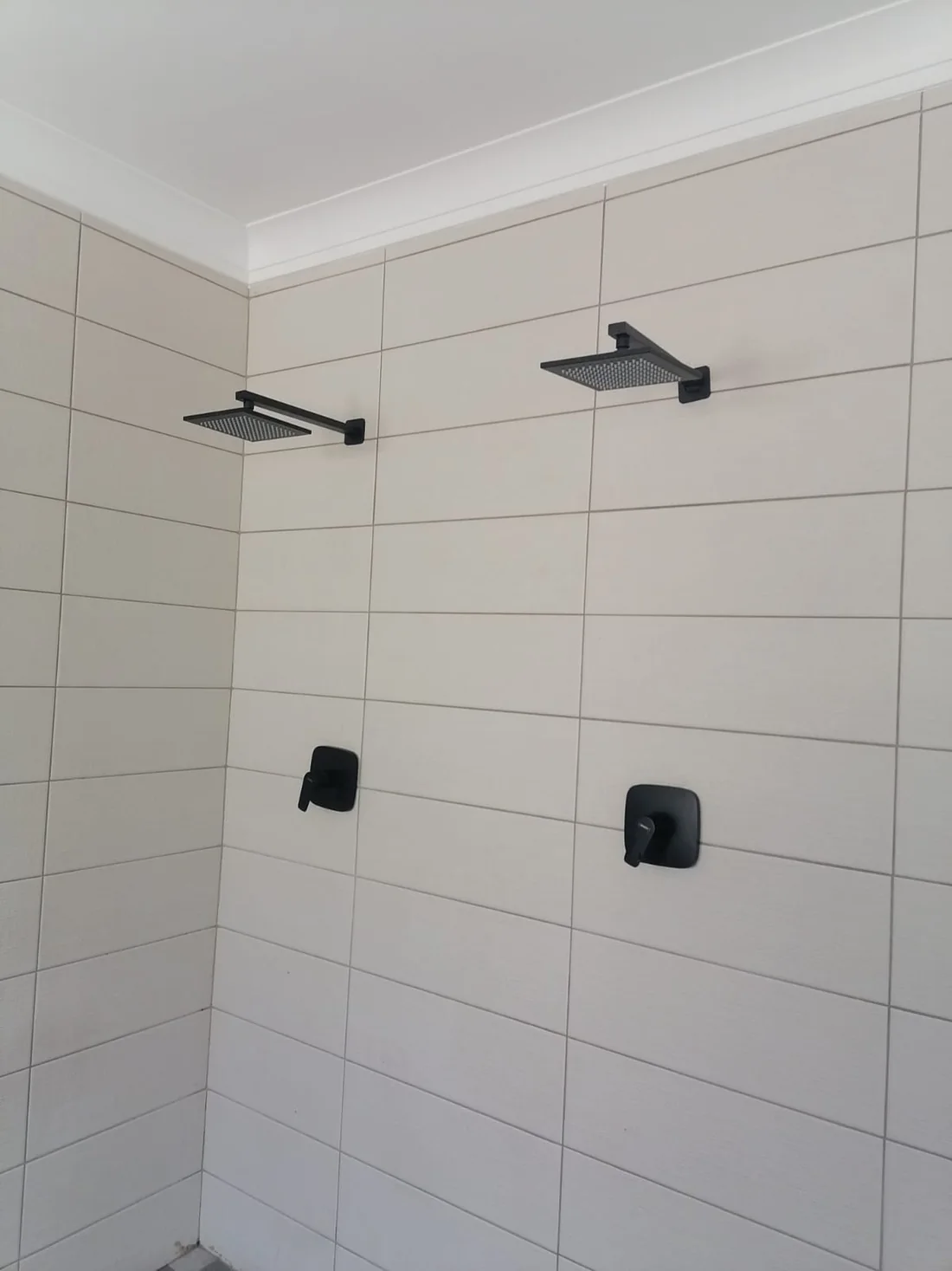 Two black square shower heads replaced in a tiled Blairgowrie bathroom.